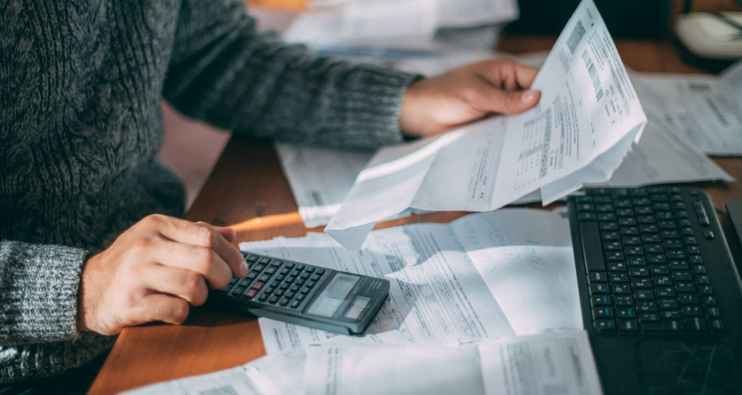 Close-up of male hands with a utility bill, a lot of checks and a calculator on the table. The man considers the costs of gas, electricity, heating. The concept of increasing tariffs for services
